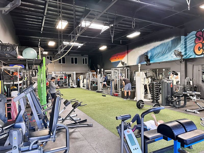 Wide view of strength machines and turf under a colorful wall mural.